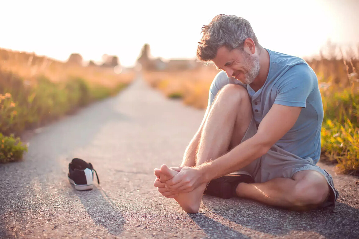Runner sitting on path holding foot due to achilles pain